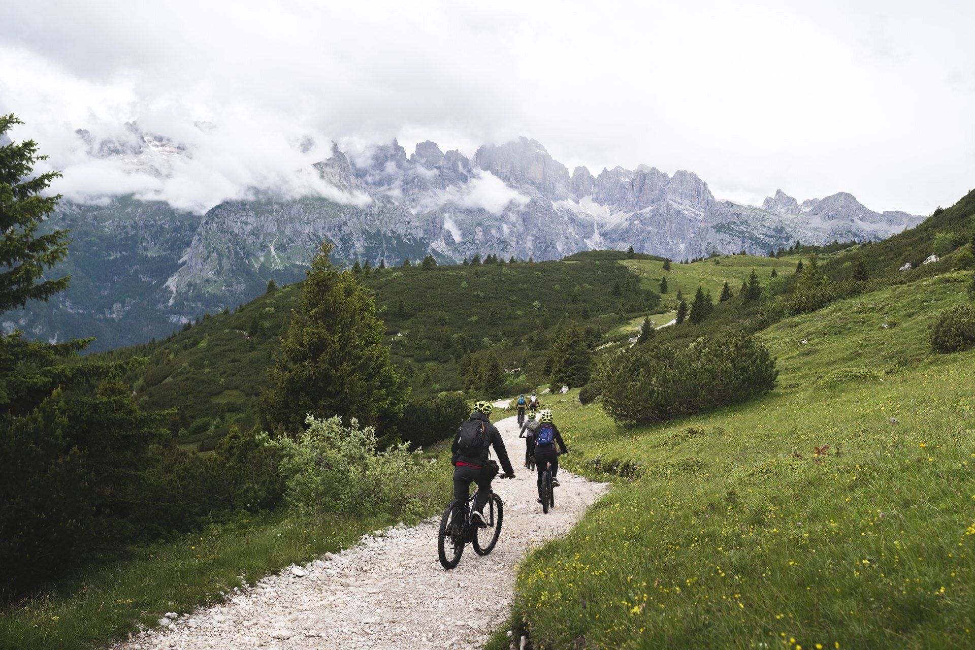 Eine Gruppe von fünf Radfahrern fährt mit ihrem e-MTB auf einem Weg auf dem Canfedin-Kamm. Im Hintergrund sind die Brenta-Dolomiten zu sehen, die durch den Nebel auftauchen. | © Marco Santinelli, 2022