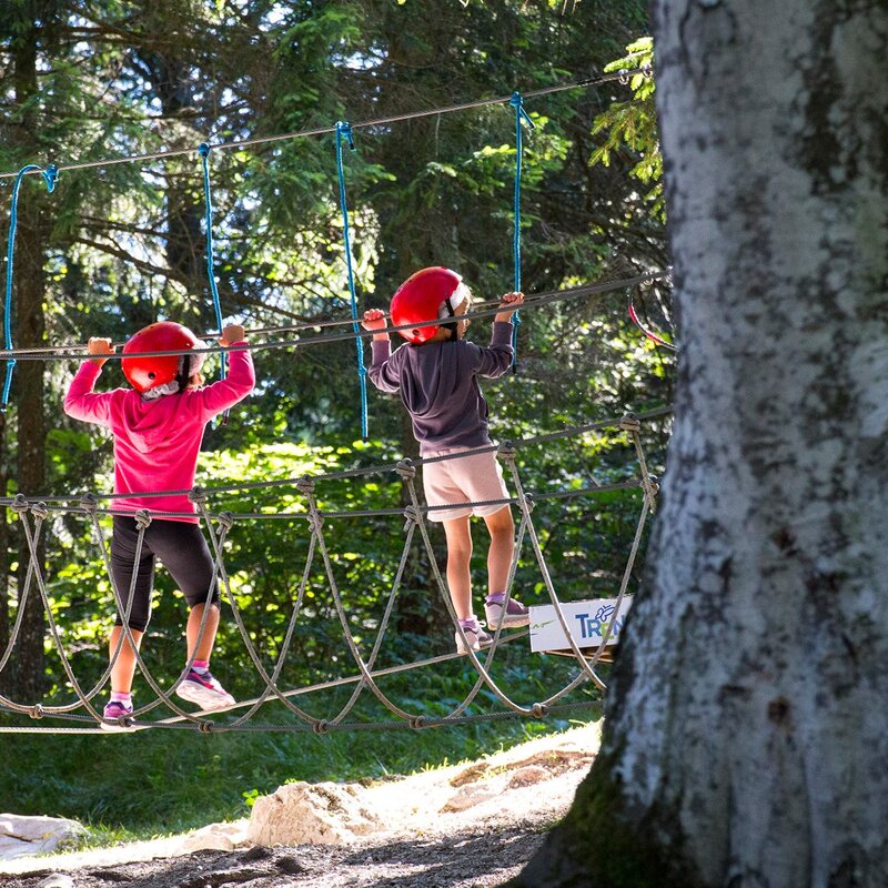 Two children with harnesses are walking on a metal lanyard that joins two plants in the forest park on the Pradel plateau, above Molveno | © Filippo Frizzera, 2019