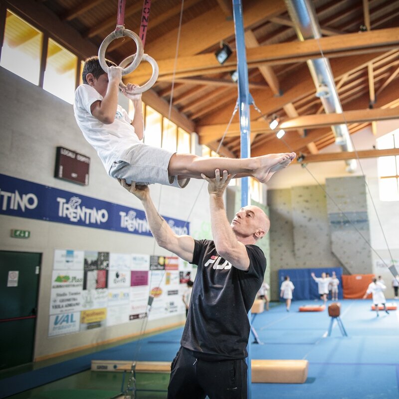 Jury Chechi, campione di ginnastica artistica, aiuta un bambino all'eserizio degli anelli. | © Federico Modica, 2017
