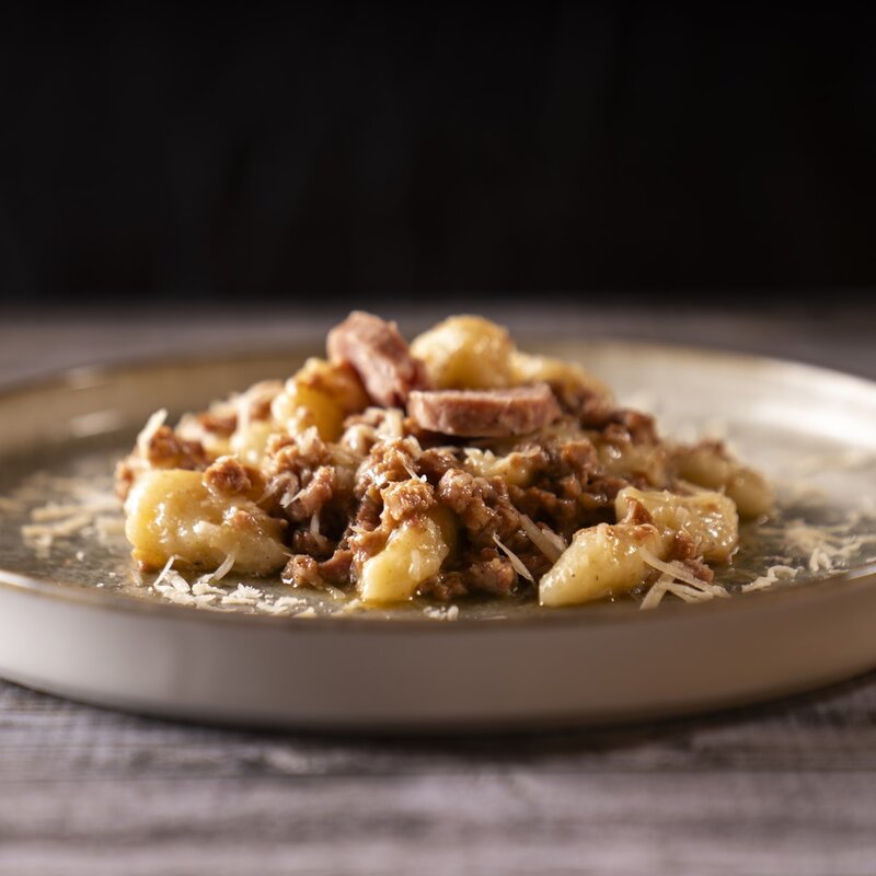 Piatto di gnocchi di patate conditi con ragù ricco, rondelle di Ciuìga e abbondante formaggio grattugiato. | © Stefano Caffarri, 2025