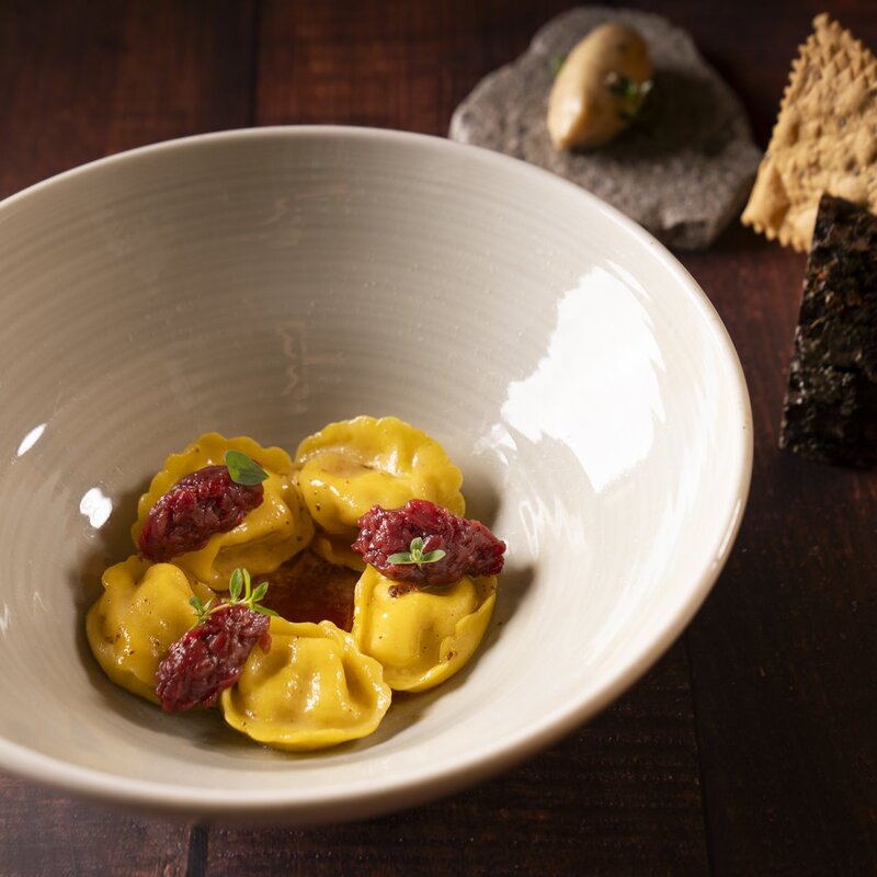 Ravioli con sedano rapa alla brace, infuso alle bacche di sambuco e crudo di cervo nostrano, serviti con cracker di segale e burro al fieno. | © Stefano Caffarri, 2025 