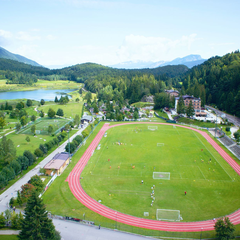 Luftaufnahme des Andalo Life Parks in Paganella. Zu sehen sind insbesondere der Fußballplatz mit der Leichtathletikbahn und seinen Parkplätzen, der Fußballplatz, die Reithalle und der Andalo-Teich | © Arch. Andalo Gestioni, 2014