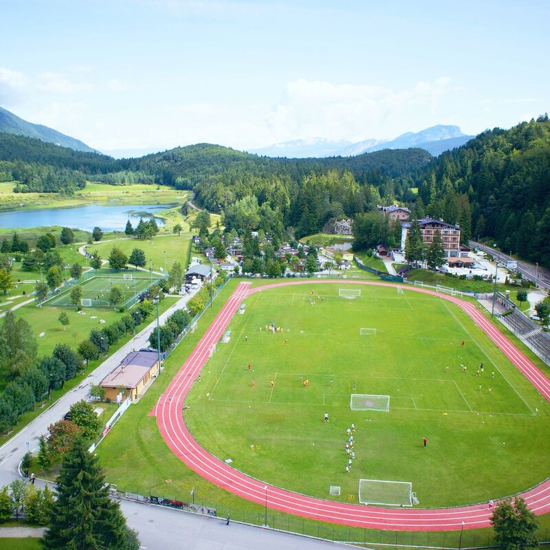 Aerial view of the Andalo Life park in Paganella. In particular, one can see the football field with the athletics track and its parking areas, the football field, the riding hall and the Andalo pond | © Arch. Andalo Gestioni, 2014
