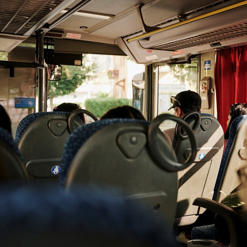 Vista interna di un autobus, inquadratura dal retro verso la parte anteriore. I passeggeri sono seduti ai loro posti, illuminati dalla luce del sole che entra dai finestrini laterali. | © Origami, 2026