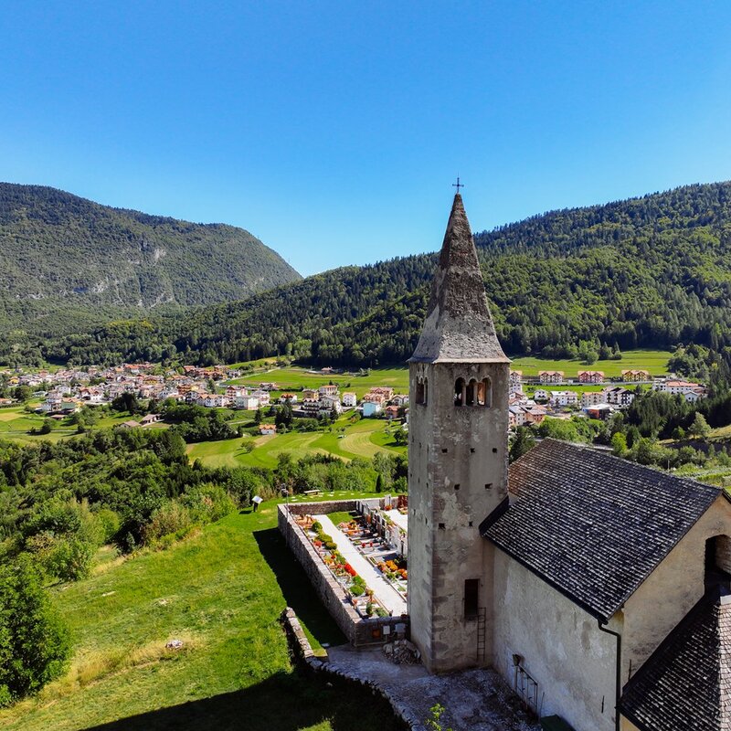 In the foreground you can see the small church of St Thomas in Cavedago. Behind there are some houses of the village and in the background evergreen forests. | © 2022