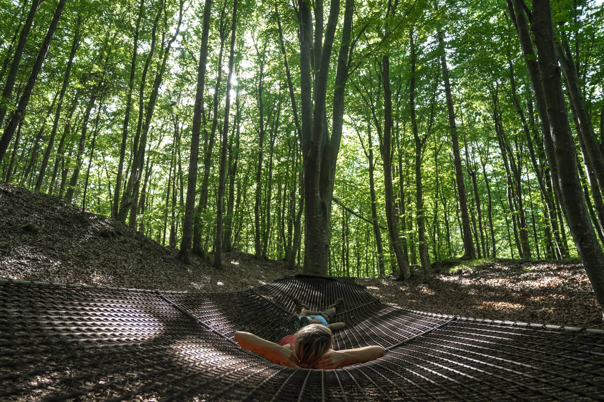 Una coppia è sdraiata sull'amaca gigante all'interno del Parco del Respiro di Fai della Paganella | © @marcosantinelli, 2022