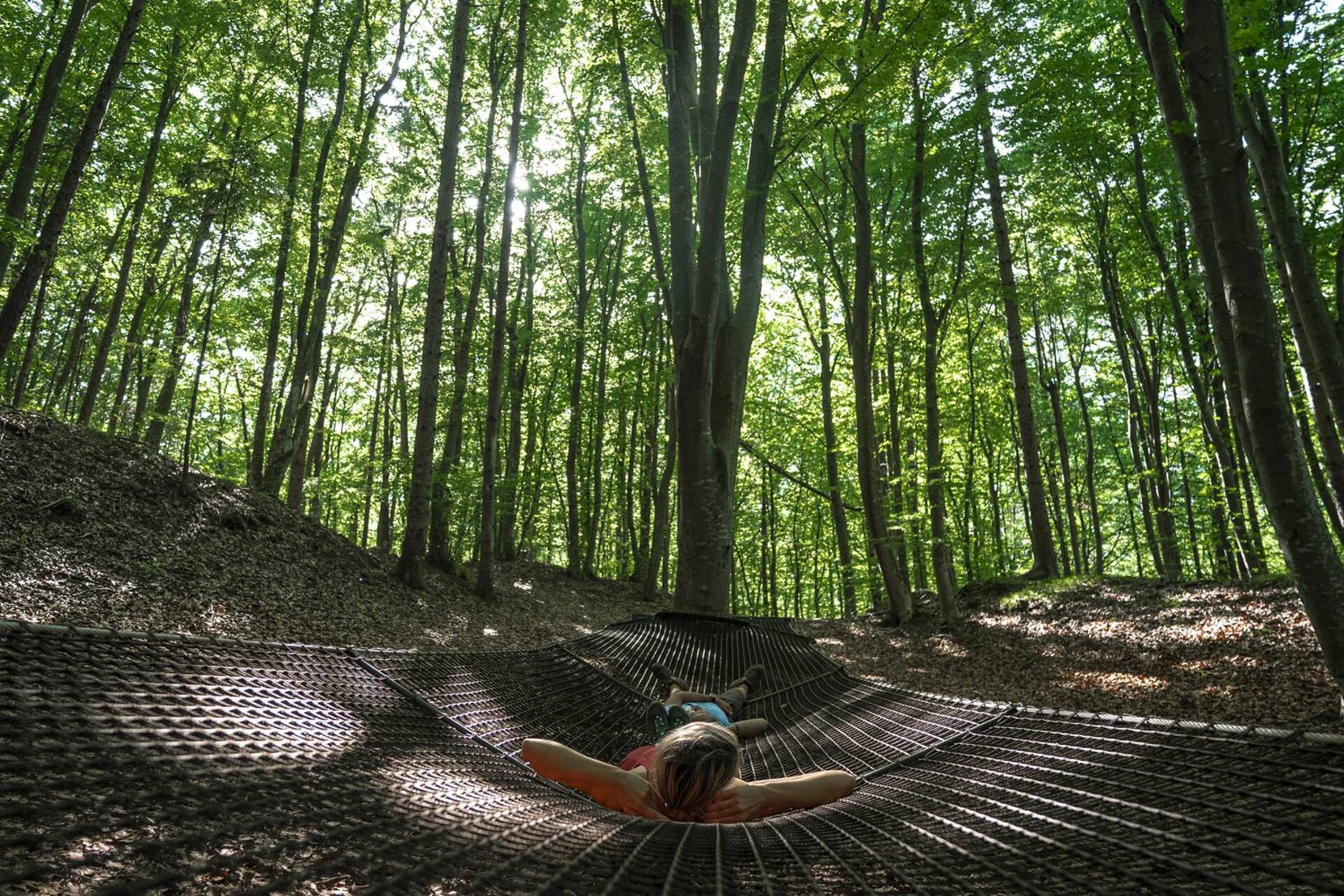 A couple is lying on the giant hammock inside the Fai della Paganella Parco del Respiro | © @marcosantinelli, 2022