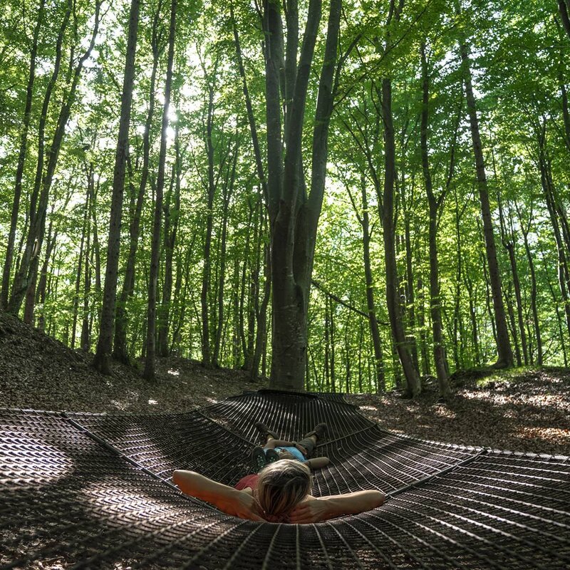 Una coppia è sdraiata sull'amaca gigante all'interno del Parco del Respiro di Fai della Paganella | © @marcosantinelli, 2022