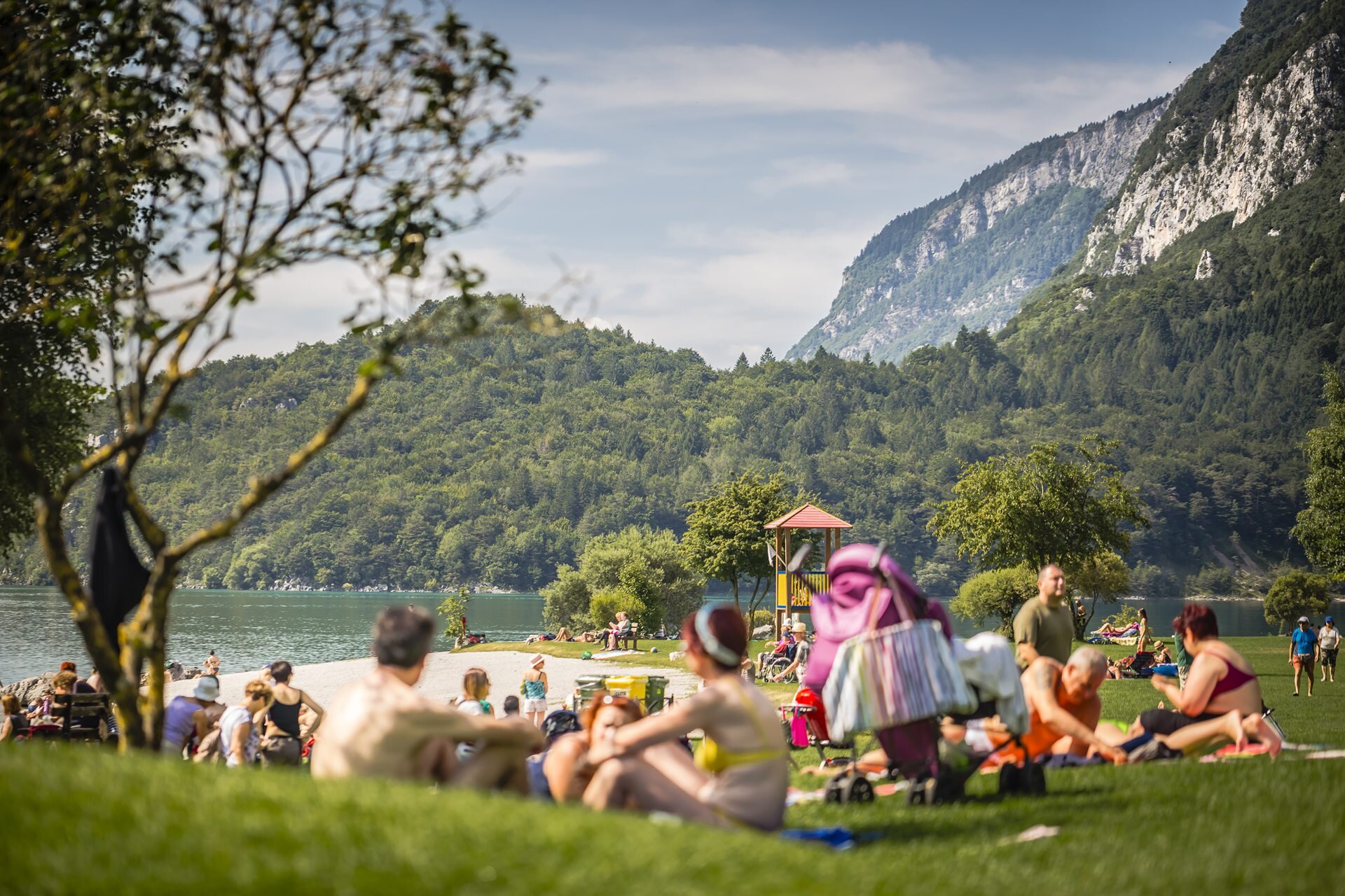 Sulla spiaggia del lago di Molveno ci sono persone sedute che prendono il sole o fanno un pic-nic, altre passeggiano, qualcuno si prepara per fare il bagno | © Story Travelers, 2016