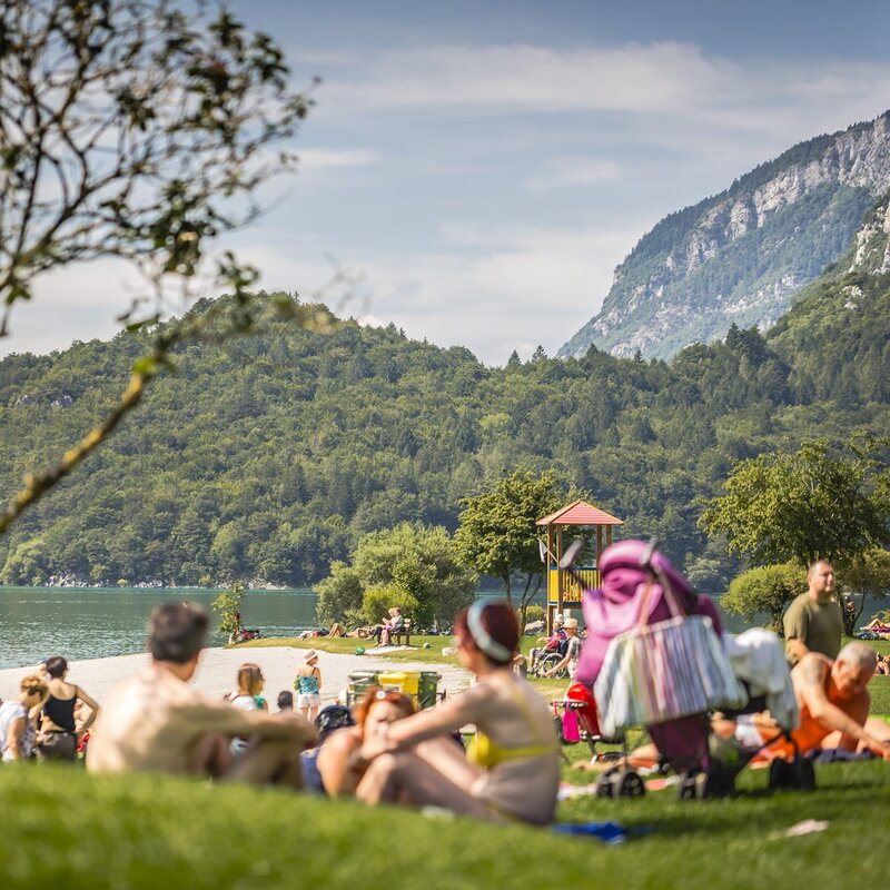 Sulla spiaggia del lago di Molveno ci sono persone sedute che prendono il sole o fanno un pic-nic, altre passeggiano, qualcuno si prepara per fare il bagno | © Story Travelers, 2016