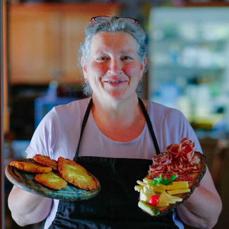 A smilingly lady displays potato tortel and a board of Trentino cold cuts and cheeses | © Vitaly Yarosh, 2022