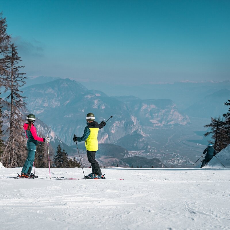 Two skiers on La Rocca slope. Below, the village of Fai della Paganella and the Adige Valley. | © Camilla Pizzini, 2022