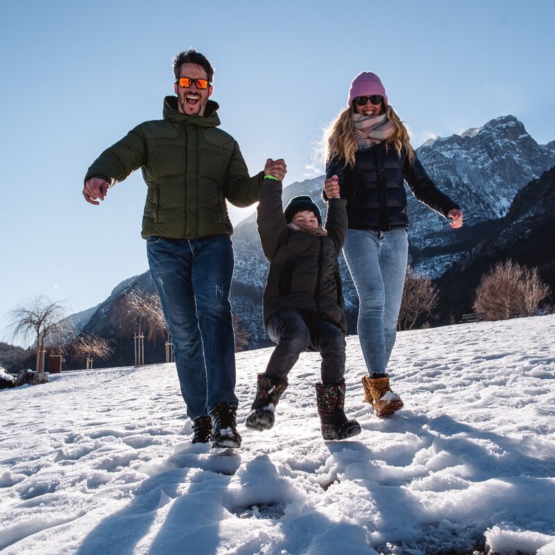 Bambino gioca con i genitori sulla riva del lago di Molveno innevata. | © Alice Russolo, 2022