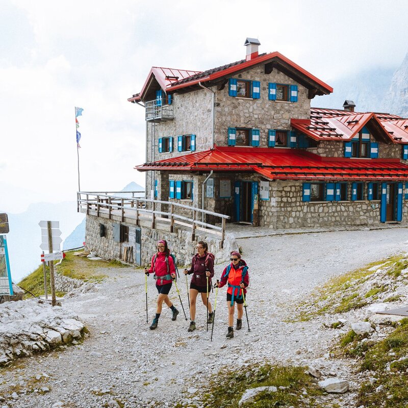 Tre ragazze camminano con bastoncini da trekking davanti al rifugio Agostini, nel cuore delle Dolomiti di Brenta | © Nicola Cagol, 2021
