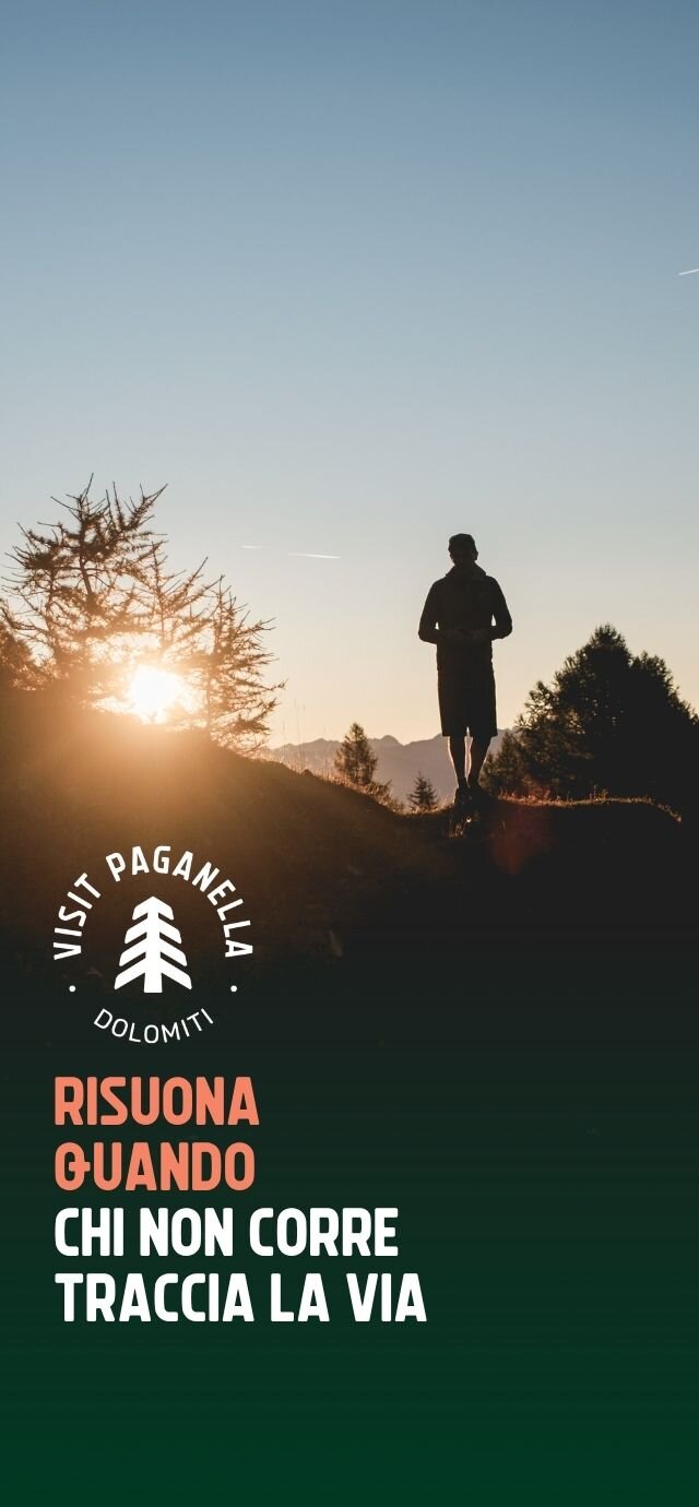 Immagine verticale con la silhouette di un uomo al tramonto sulle Dolomiti. Sono presenti il logo "Visit Paganella Dolomiti" e la scritta "RISUONA QUANDO CHI NON CORRE TRACCIA LA VIA". | © Filippo Frizzera, 2025