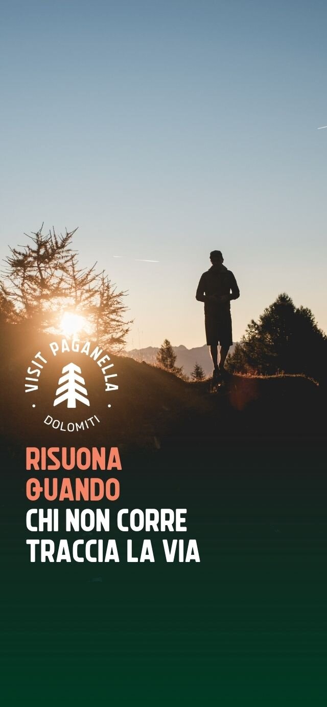Immagine verticale con la silhouette di un uomo al tramonto sulle Dolomiti. Sono presenti il logo "Visit Paganella Dolomiti" e la scritta "RISUONA QUANDO CHI NON CORRE TRACCIA LA VIA". | © Filippo Frizzera, 2025