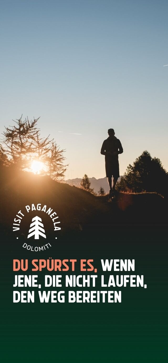 Vertikale Werbegrafik mit der Silhouette eines Mannes im Gegenlicht der Abendsonne in den Bergen. Enthalten sind das "Visit Paganella Dolomiti"-Logo und der Spruch: "DU SPÜRST ES, WENN JENE, DIE NICHT LAUFEN, DEN WEG BEREITEN". | © Du spürst es, wenn jene, die nicht laufen, den Weg bereiten