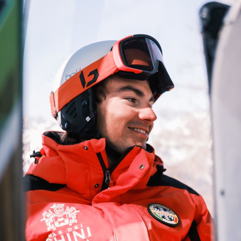 Imparare a sciare in Paganella | © Filippo Frizzera, 2025 Ritratto in primo piano di un maestro di sci sorridente sulle piste della Paganella. Indossa casco, maschera da sci appoggiata sul casco e la divisa rossa della scuola di sci. | © Filippo Frizzera, 2025