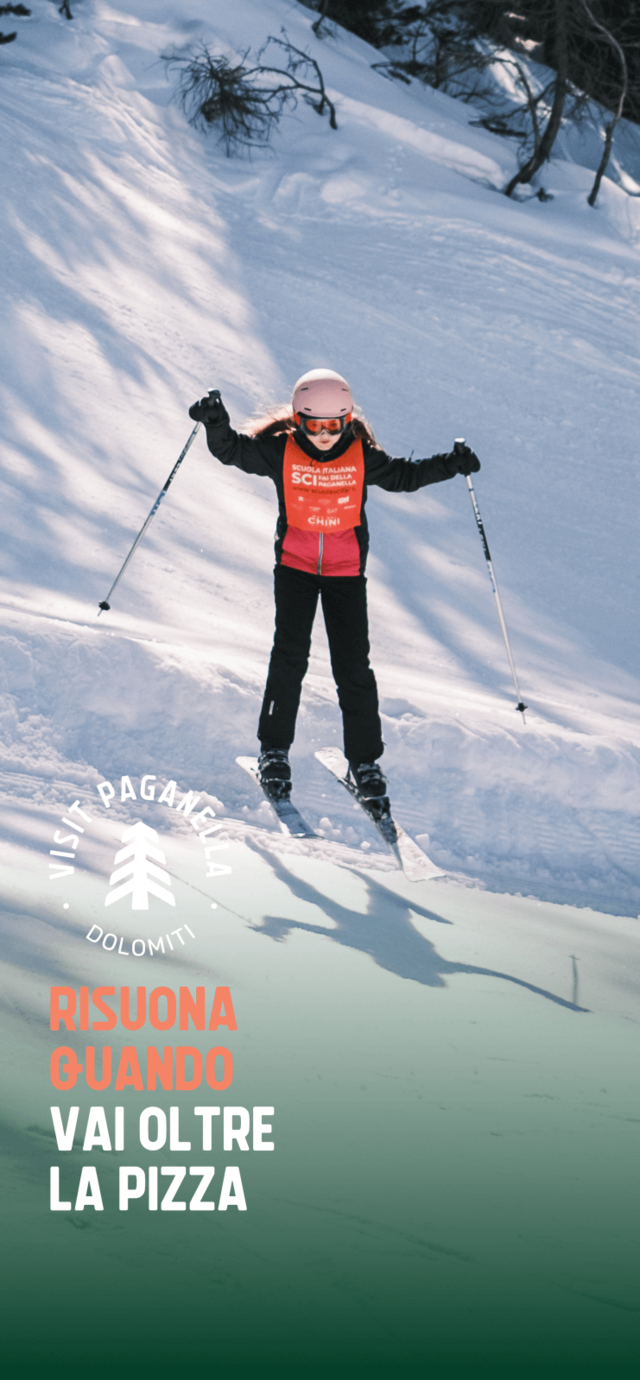 Una bambina scia con sicurezza su una pista innevata della Paganella, indossando casco, occhiali da sci e una pettorina arancione della scuola di sci. Il testo in sovrimpressione dice "RISUONA QUANDO VAI OLTRE LA PIZZA". | © Filippo Frizzera, 2025