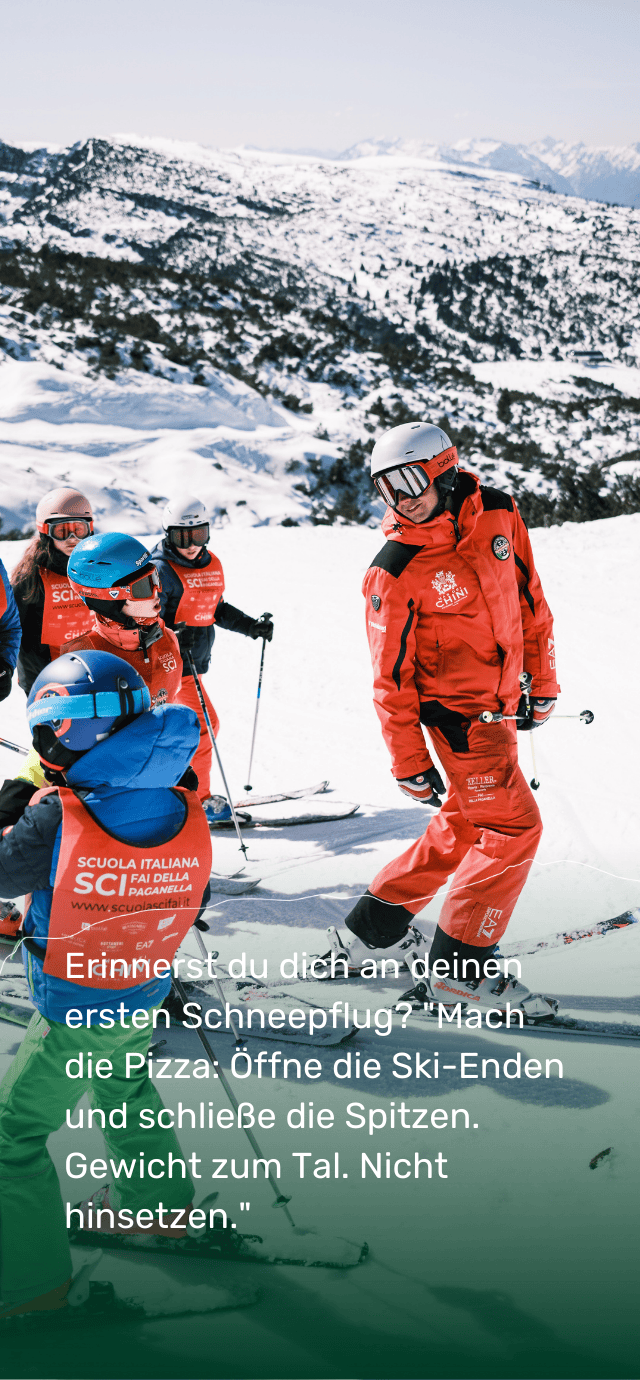 Ein Skilehrer aus Paganella in roter Uniform zeigt einer Gruppe von Kindern während einer Skistunde die Skitechnik. Im Hintergrund eröffnet sich ein weitläufiger Blick auf verschneite Pisten.  Überlagerter Text: Erinnerst du dich an deinen ersten Schneepflug? „Mach eine Pizza: Öffne die Schwänze und schließe die Spitzen. Gewicht talwärts. Nicht hinsetzen.“ | © Filippo Frizzera, 2025