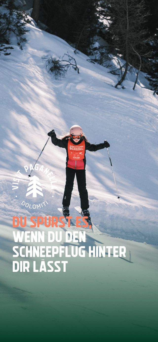 Ein kleines Mädchen fährt selbstbewusst auf einer verschneiten Piste der Paganella Ski- und Snowboardschule Ski, mit Helm, Skibrille und einer orangefarbenen Weste der Skischule. Der überlagerte Text lautet: „Du spürst es, wenn du den Schneepflug hinter dir lässt“. | © Filippo Frizzera, 2025