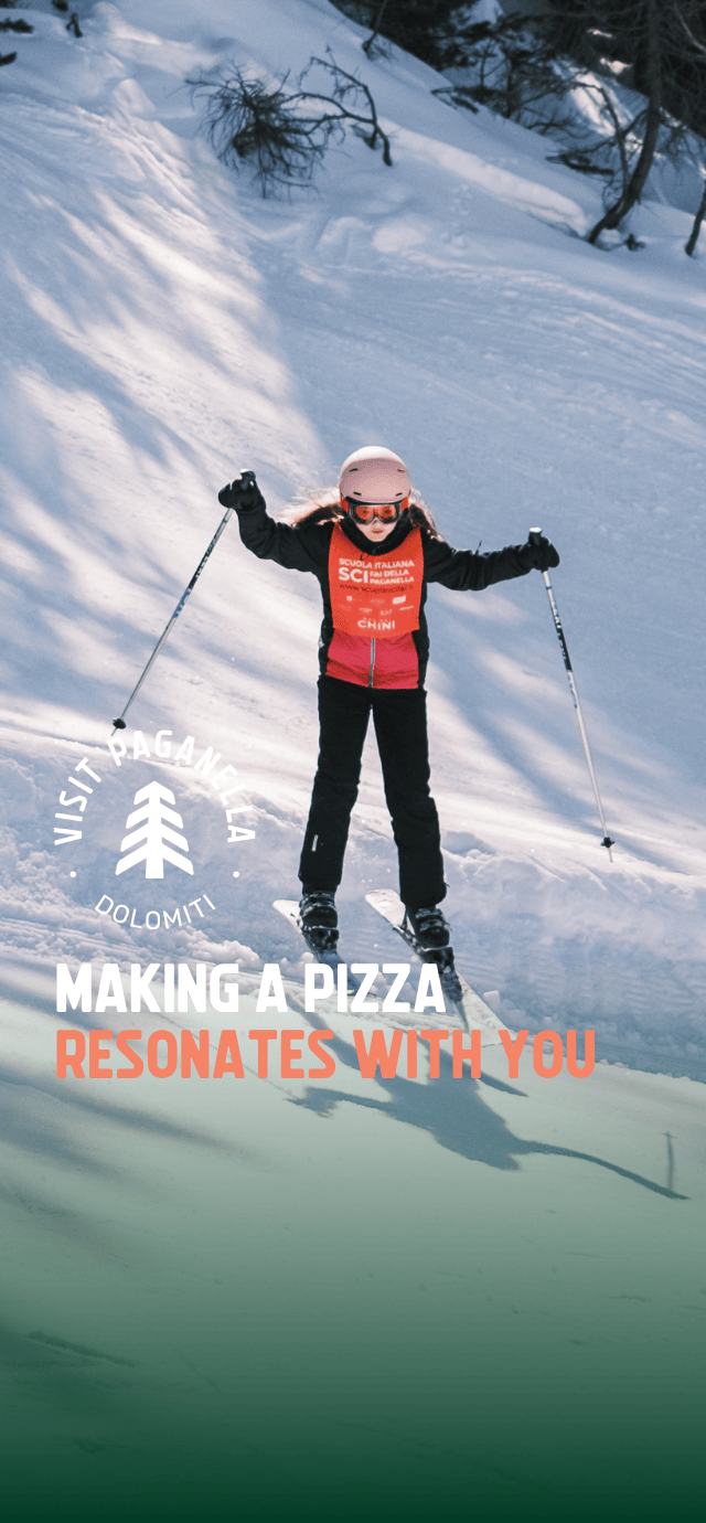 A little girl skis confidently down a snow-covered slope in Paganella, wearing a helmet, ski goggles and an orange ski school bib. Overlay text: MAKING A PIZZA RESONATES WITH YOU. | © Filippo Frizzera, 2025