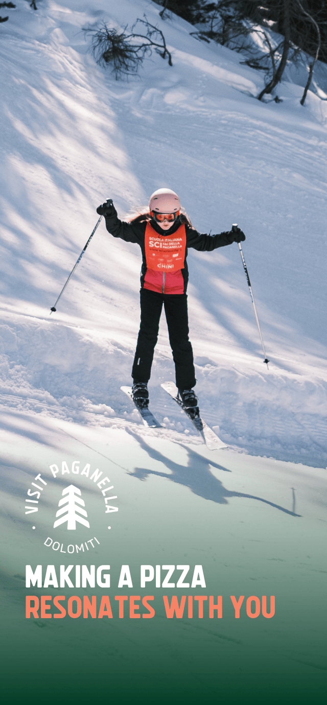 A little girl skis confidently down a snow-covered slope in Paganella, wearing a helmet, ski goggles and an orange ski school bib. Overlay text: MAKING A PIZZA RESONATES WITH YOU. | © Filippo Frizzera, 2025
